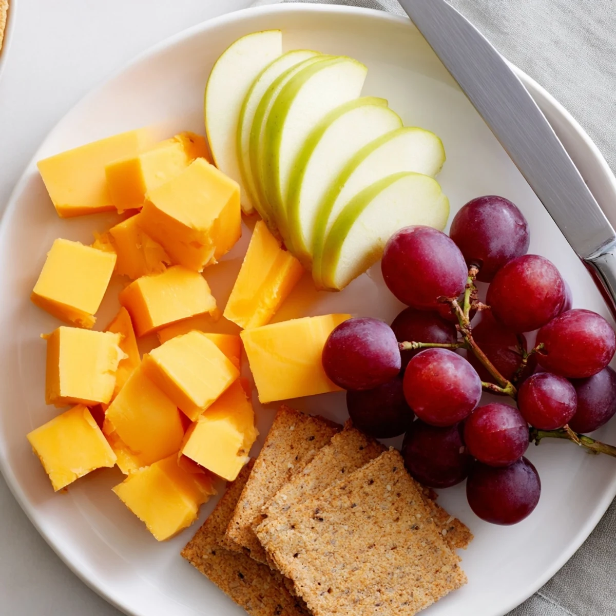 Colorful snack plate arranged with savory cheese, sweet grapes, and crisp apple slices.
