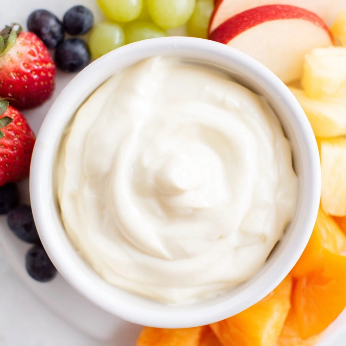 A big serving of cream cheese fruit dip, alongside a variety of colorful dipping fruits for a party.