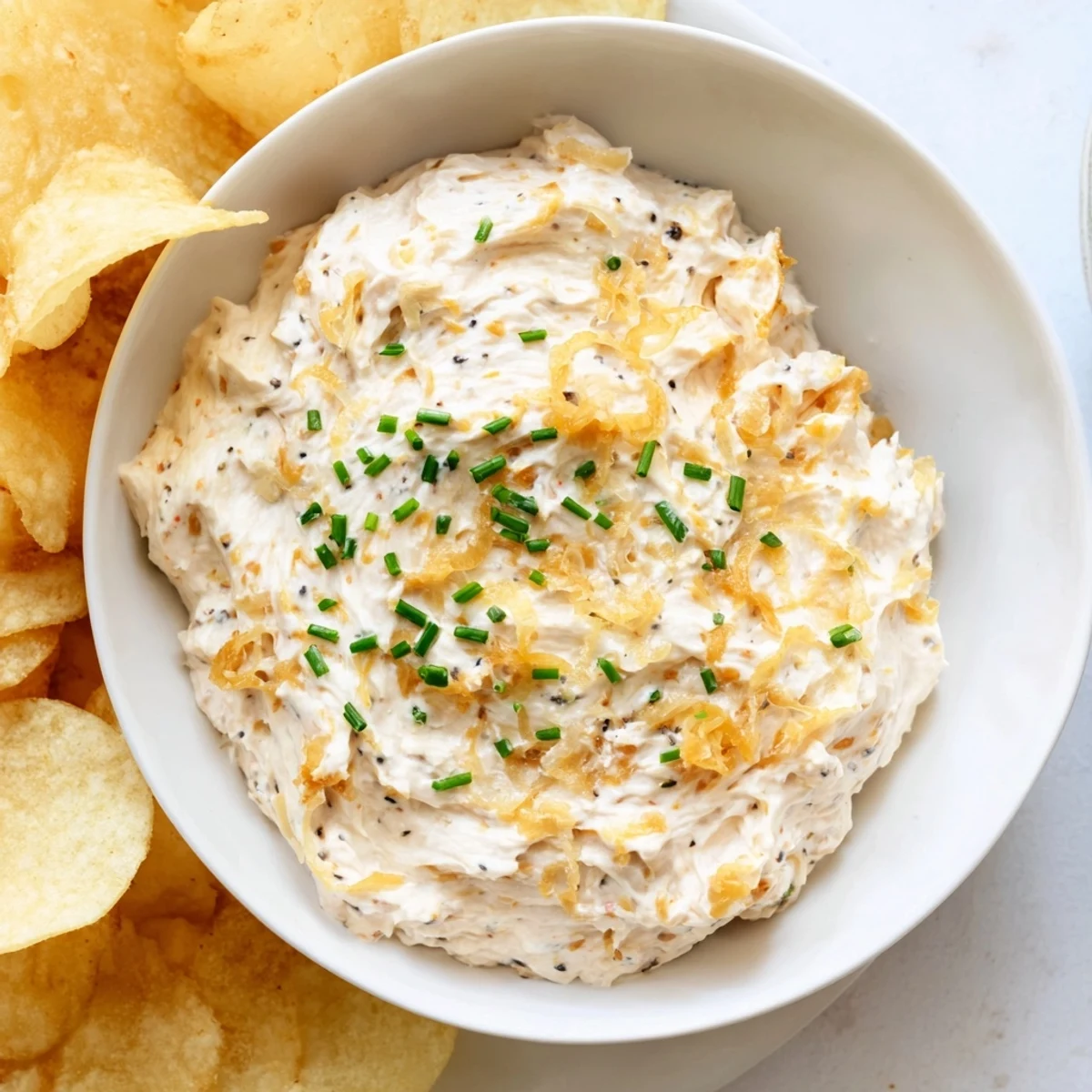Crisp potato chips surround a creamy bowl of homemade classic onion dip, ready to be enjoyed.