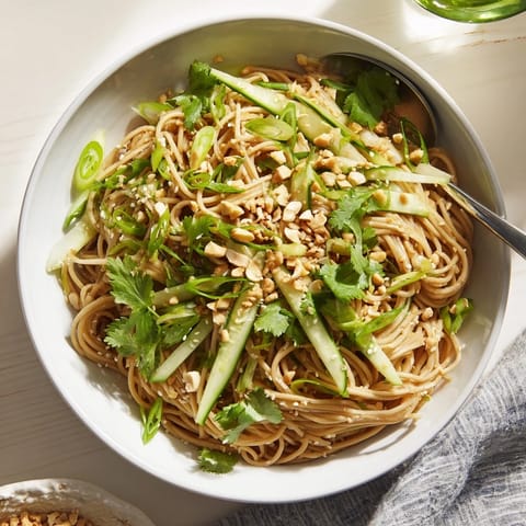 A close-up of a spicy sesame noodle salad garnished with toasted sesame seeds, sliced spring onions, and optional roasted peanuts.  