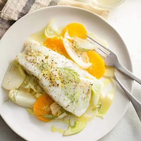 Poached Cod with Fennel and Orange on a white plate, garnished with fennel fronds and a slice of orange.  