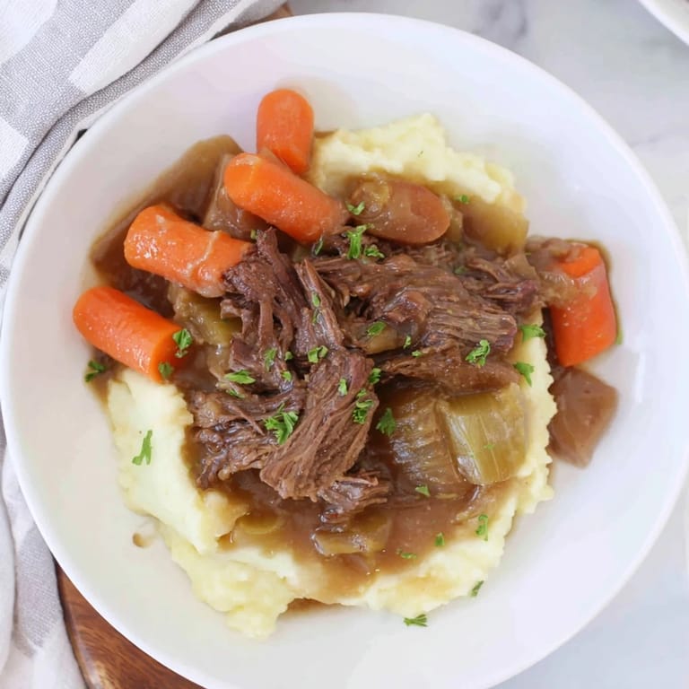 A close-up of a steaming, fork-tender pot roast atop fluffy mashed potatoes.