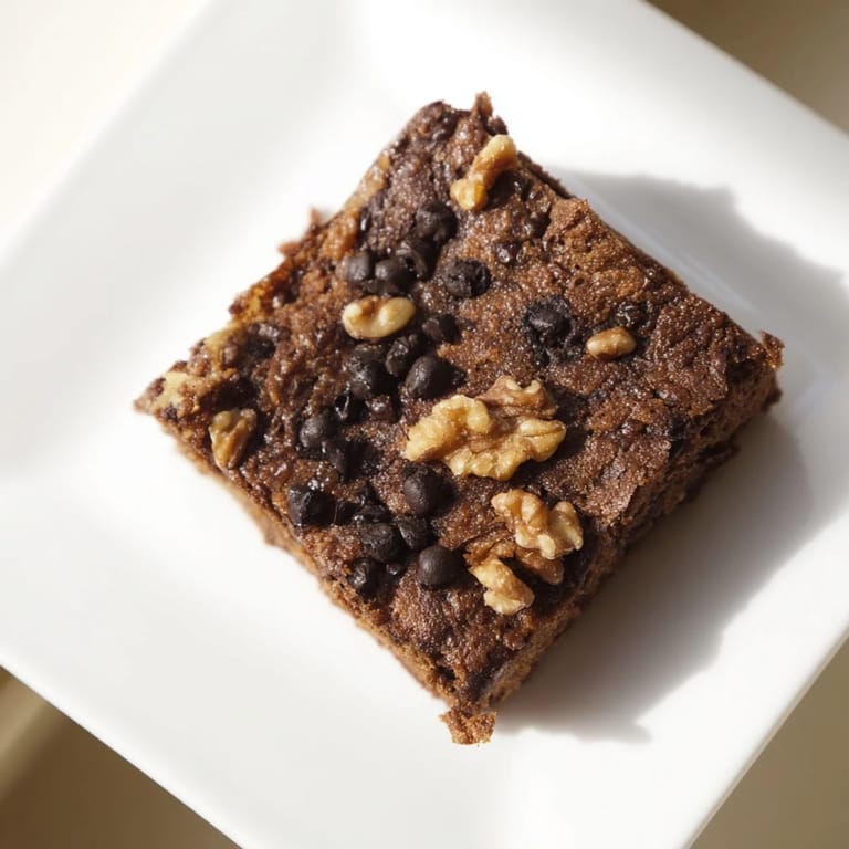 A tray of baked sweet potato brownies, featuring visible chocolate chips and a slightly cracked surface.