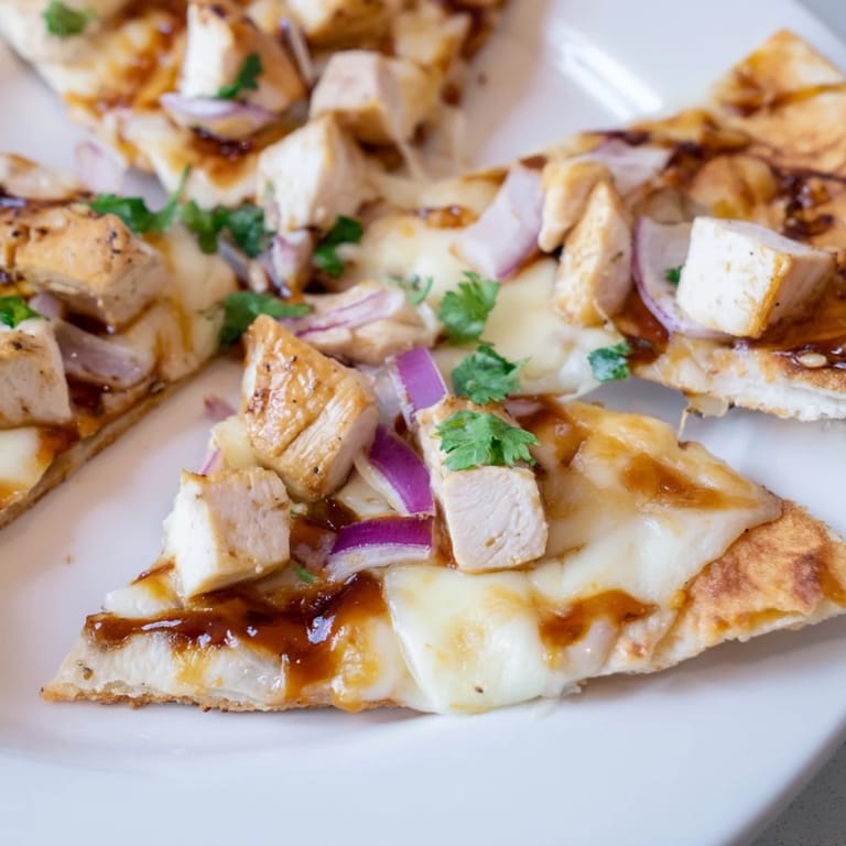 Freshly baked BBQ Chicken Flatbread served on a white plate with a side salad, drizzled with extra BBQ sauce and scattered cilantro garnish.