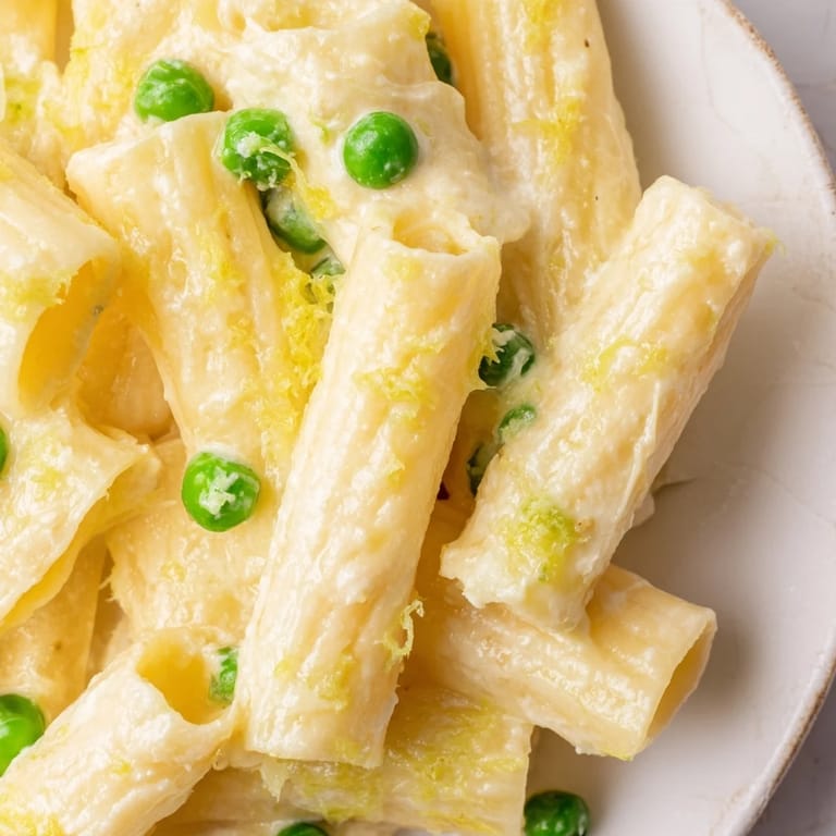 A close-up of silky Pea & Lemon Ricotta Pasta in a white bowl, showcasing lemon zest and grated Parmesan for a zesty finish.  